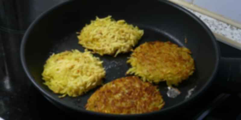 Crispy Swiss rösti patties frying in a pan, made from grated potatoes and a beloved local street delicacy.