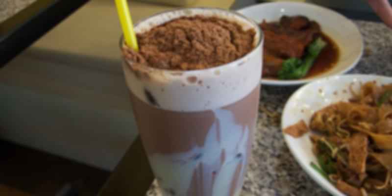 Chilled Milo Dinosaur drink topped with a heap of Milo powder, served alongside a local meal.