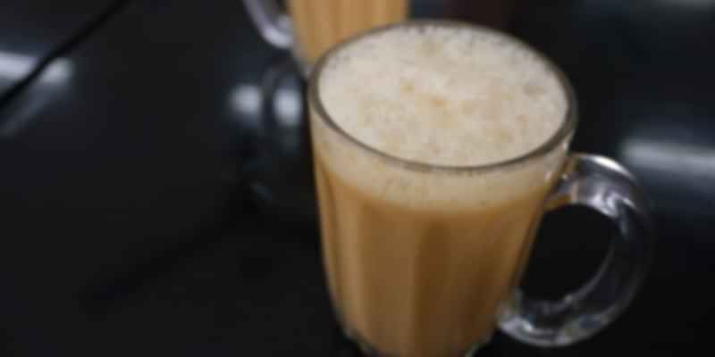 Frothy Teh Tarik milk tea served hot in a glass mug on a stainless steel counter.