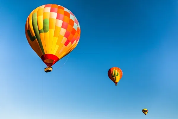 Colourful hot air balloons soaring through a clear blue sky during the best time for a hot air balloon ride in Dubai, offering spectacular sunrise views over the desert.