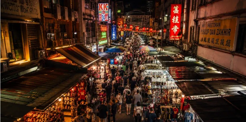 Bustling Chinatown night market alley in Petaling Street with vibrant shopfronts and pedestrians.