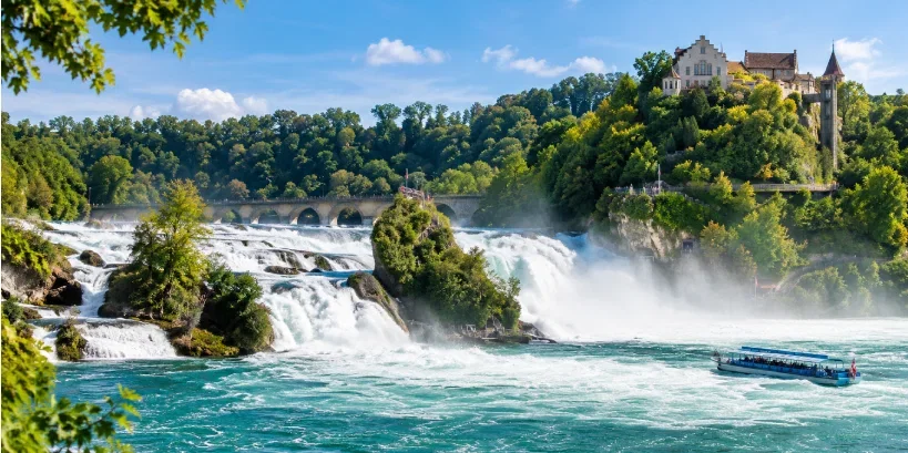 Rhine Falls cascading through the Rhine River in Switzerland, surrounded by lush greenery and rocky cliffs.